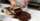 A chef uses a spatula to shear melted chocolate on a marble slab
