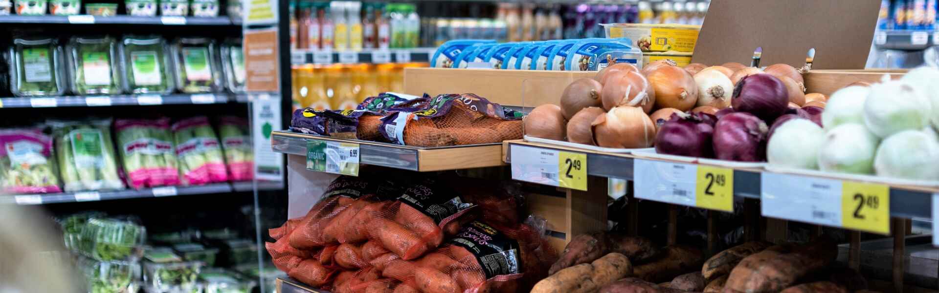 Onions and sweet potatoes are displayed in a grocery store produce area