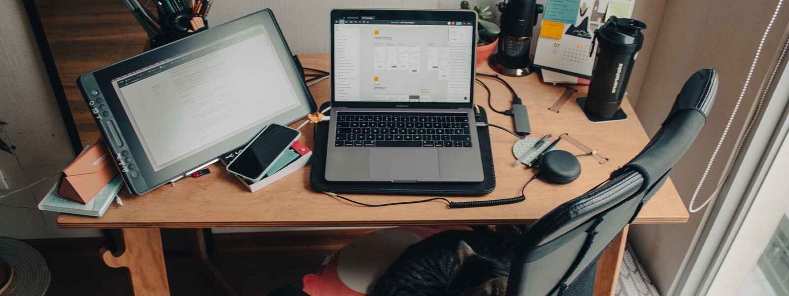 A work from home set up with a laptop and tablet, and office accessories, on a desk.