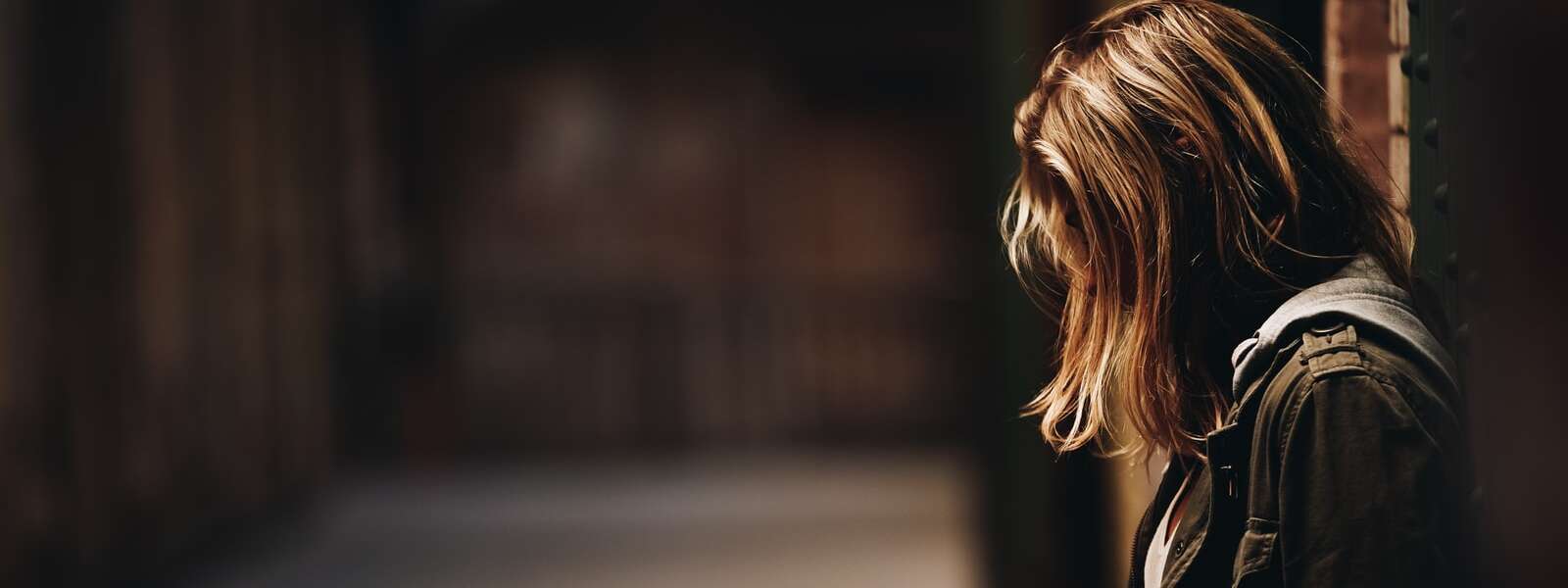 A person leaning against a wall in dim hallway