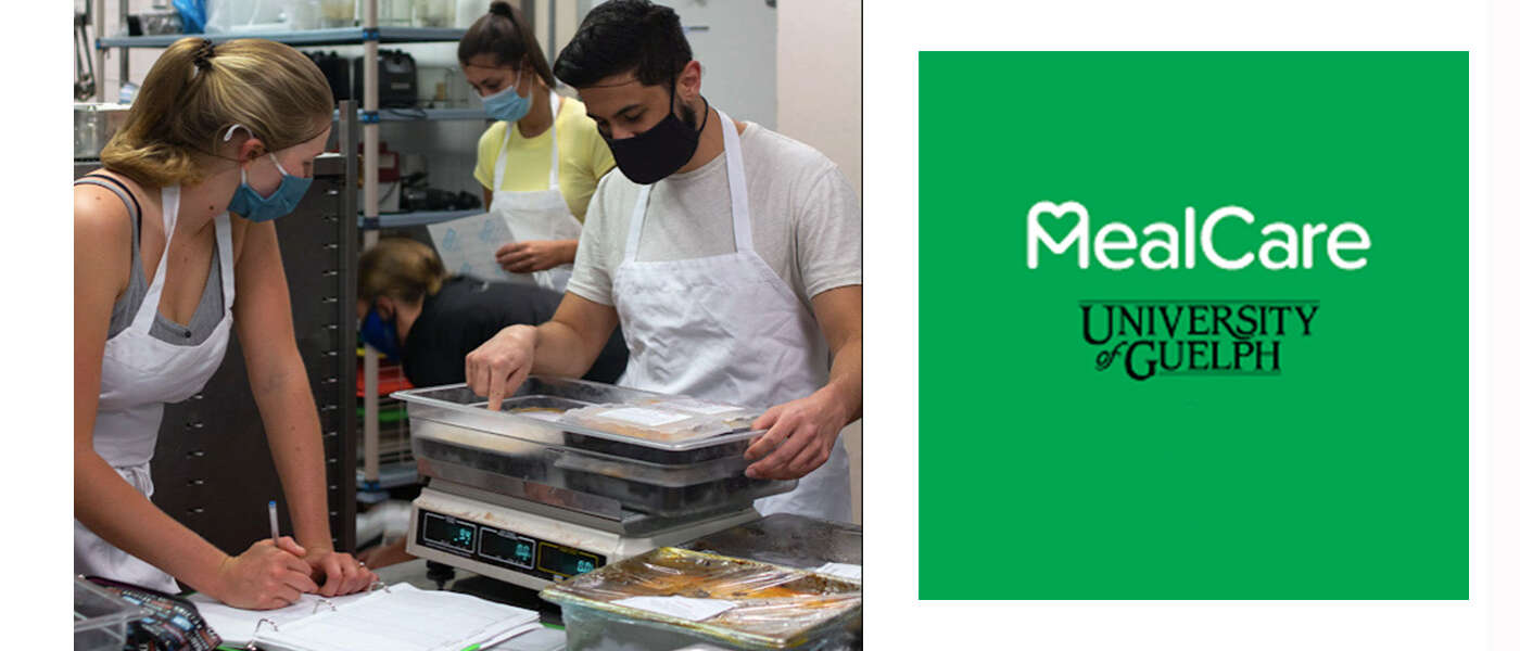 Two people wearing aprons and masks prepare meal trays in a commercial kitchen
