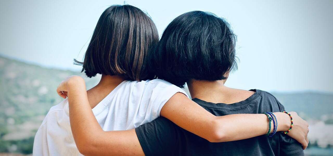 Two women are seen from behind with their arms over each others' shoulders