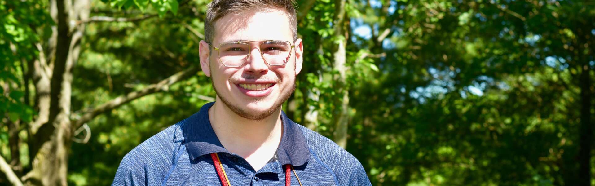 Brad Howie stands in a blue shirt against a background of trees at The Arboretum.