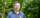 Brad Howie stands in a blue shirt against a background of trees at The Arboretum.