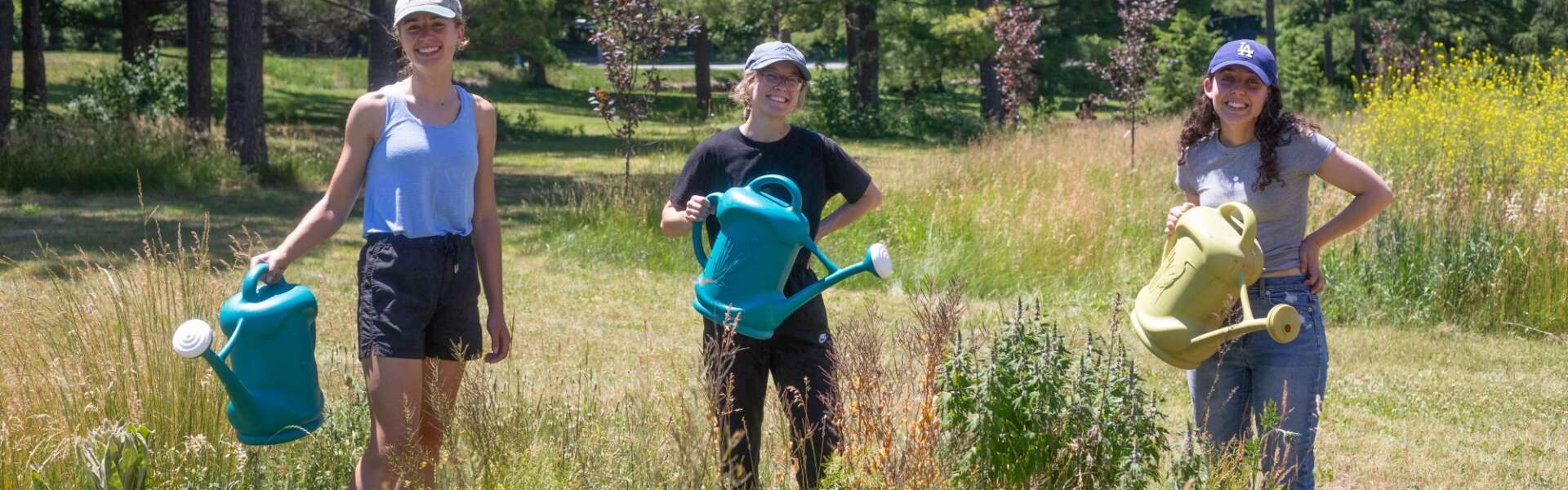 Three volunteers holding watering cans pose for a photo in a garden.