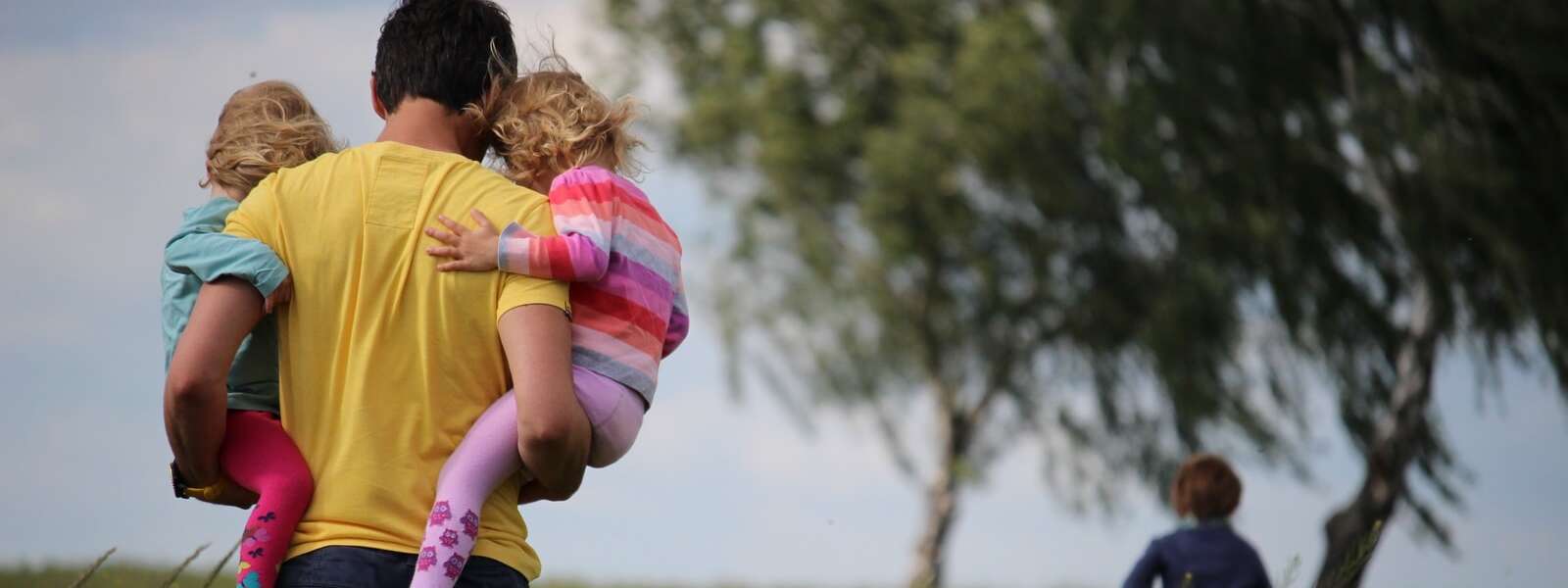 man carrying 2 young children on field of red flowers