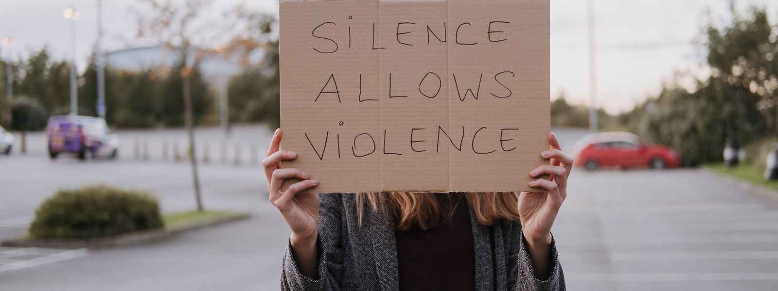 Unrecognizable woman in casual clothes standing on road and demonstrating poster Silence Allows Violence