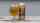 A glass of a yellow beer sits on a wooden table next to a silver can with a brown butterfly on an orange label.