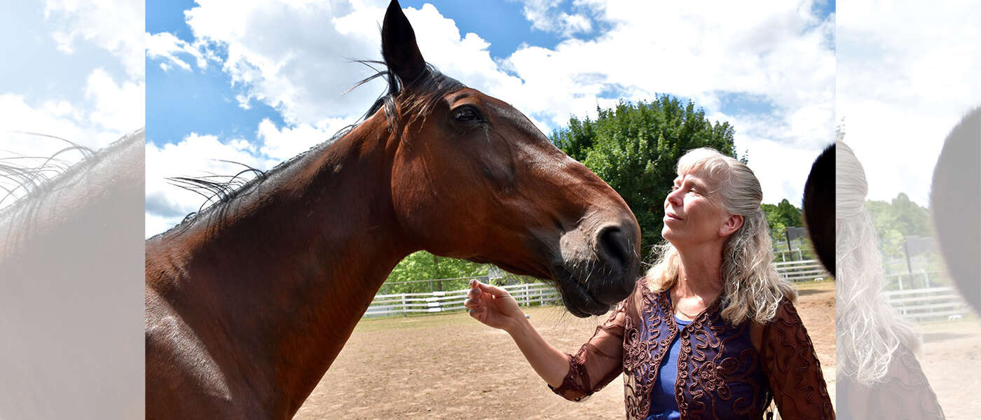 Brown horse stands with Dr. Katrina Merkies in purple shirt against a backdrop of greenery and blue sky