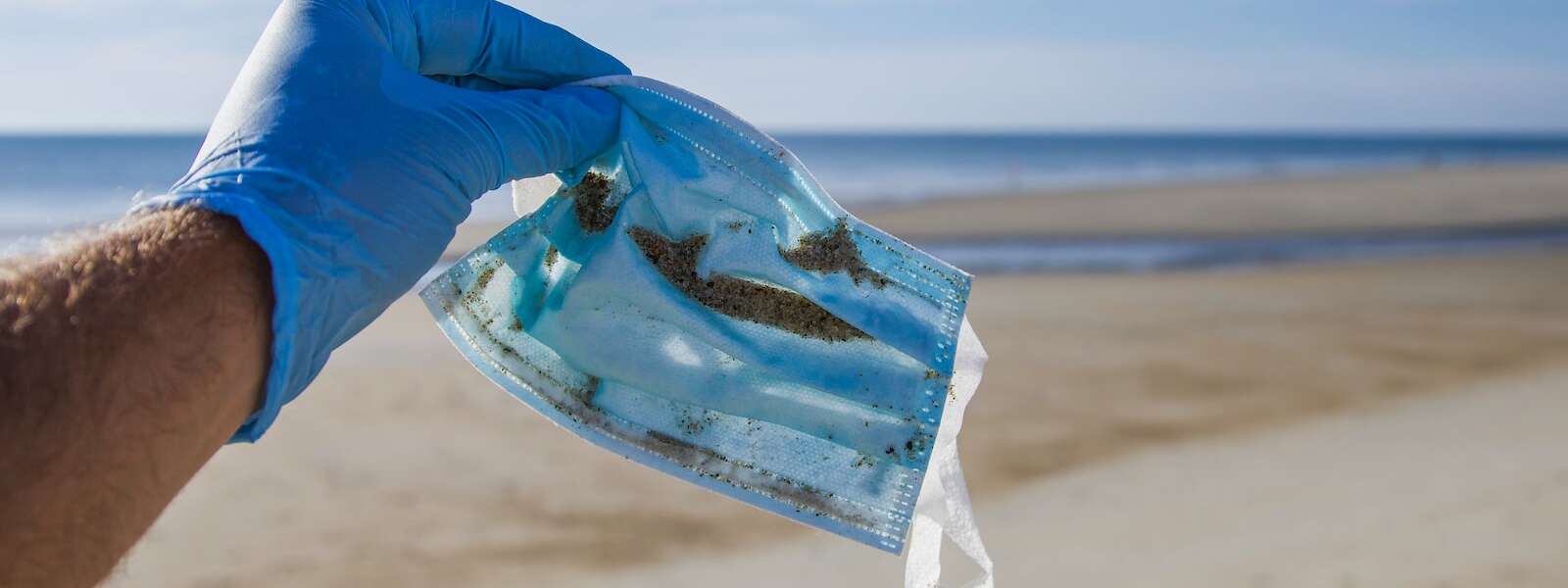 a gloved hand holds a discarded mask picked up from the beach