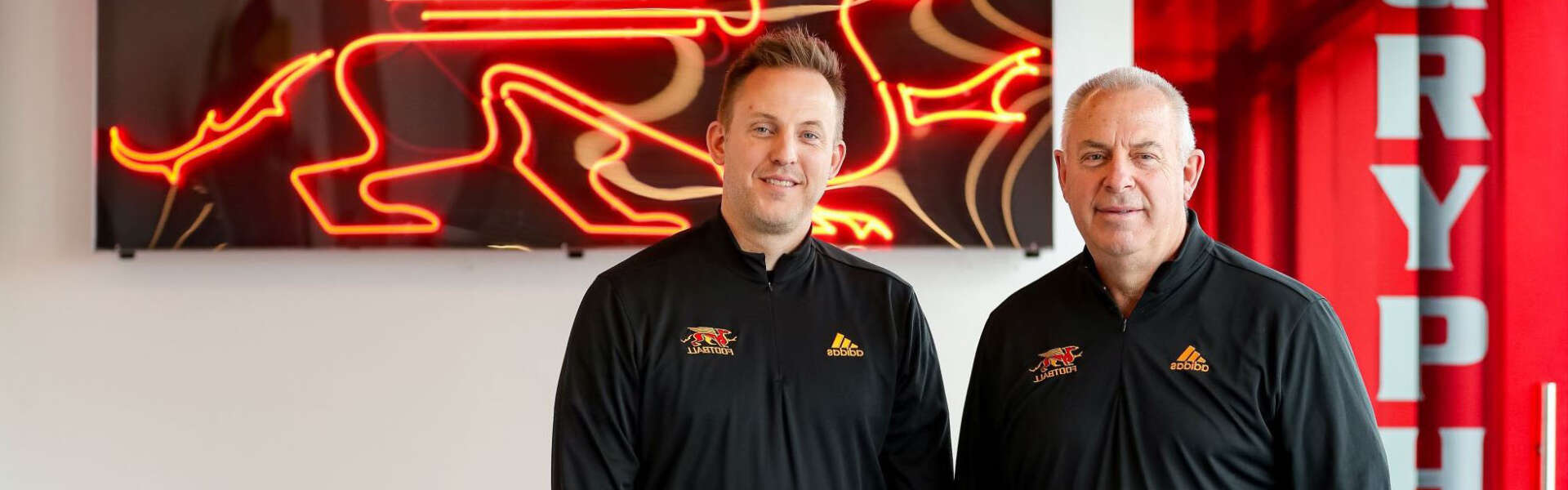 Ryan and Pat Sheahan stand against a neon Gryphons sign