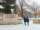 Students wearing black parkas and blue jeans walk past a beige stone sign that says "University of Guelph" during snowfall.