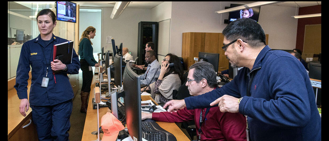 Several people look at computers, and answer phones in a health crisis centre