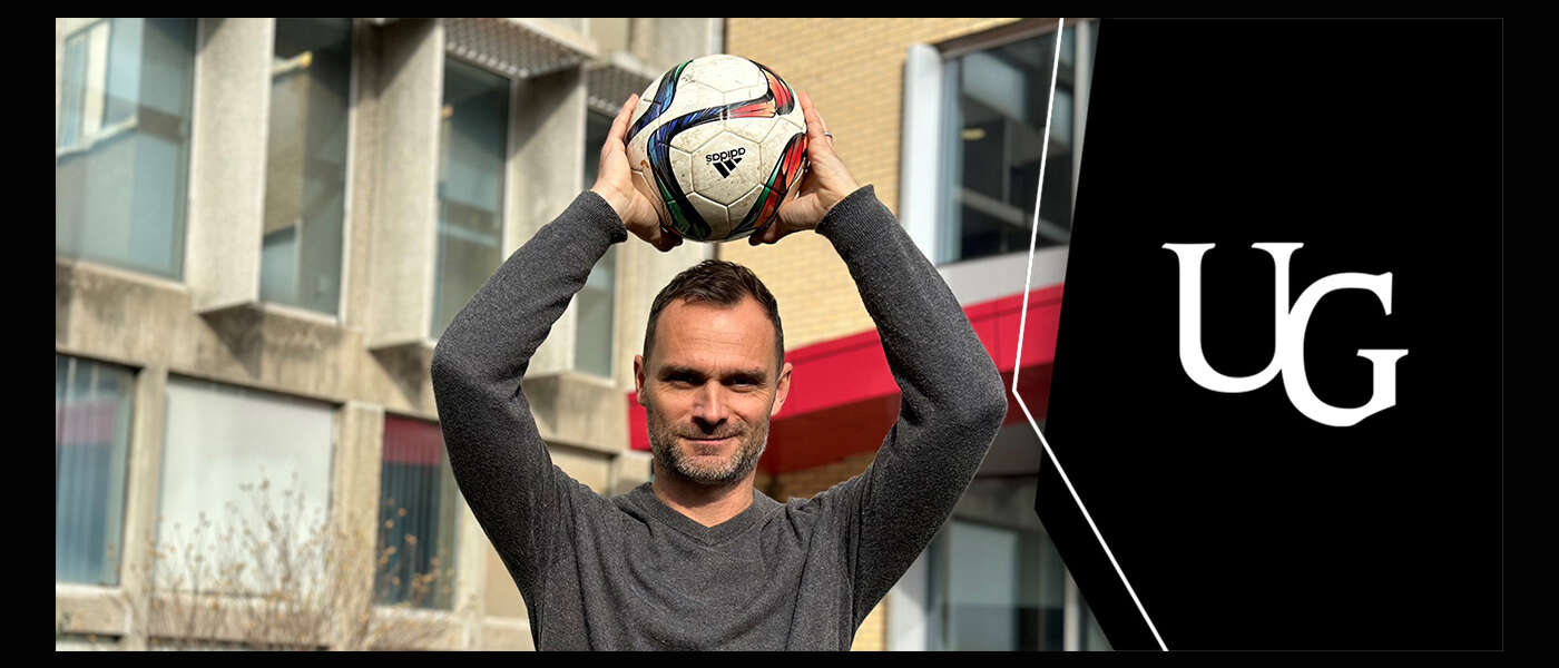 Dr. Alan McDougall holds a soccer ball over his head and smiles for the camera