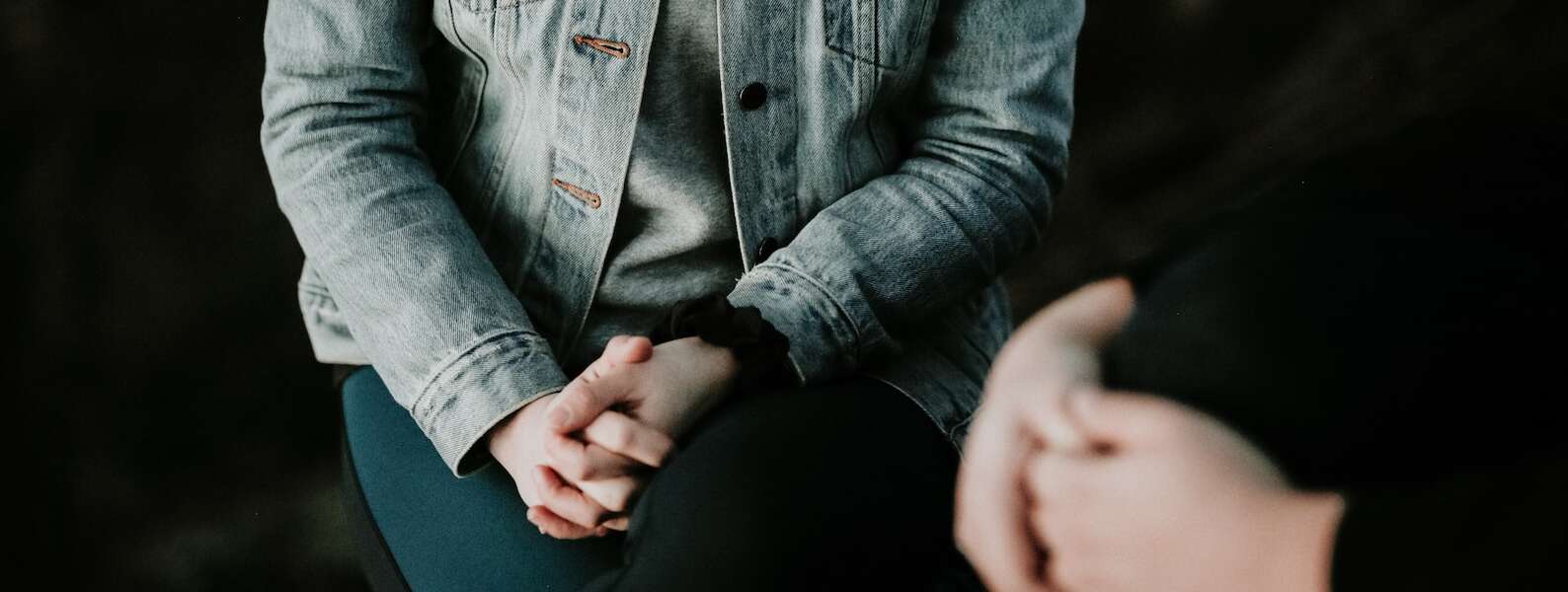 Person wearing jean jacket with ahands folded near another with hands folded