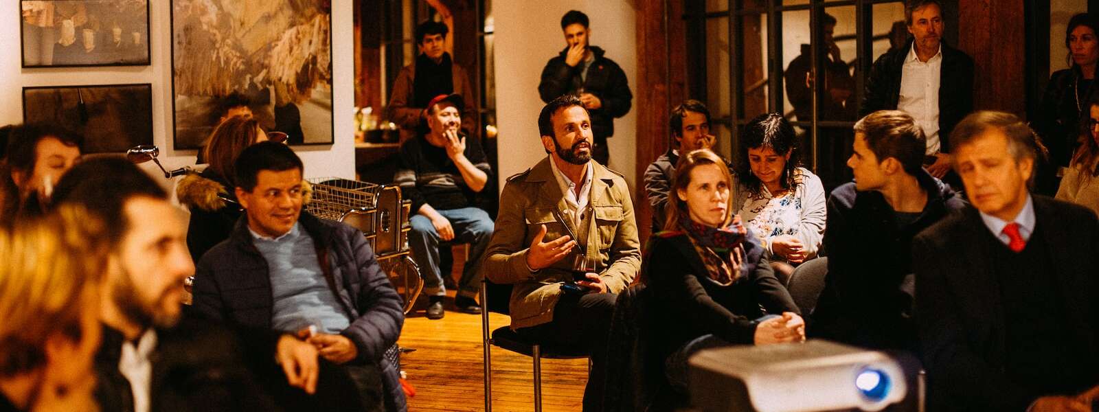 An audience member speaks as people sit in chairs watchinga slide presentation in an art gallery-like setting