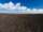A tilled field with mountains in the distance and a cloudy blue sky.