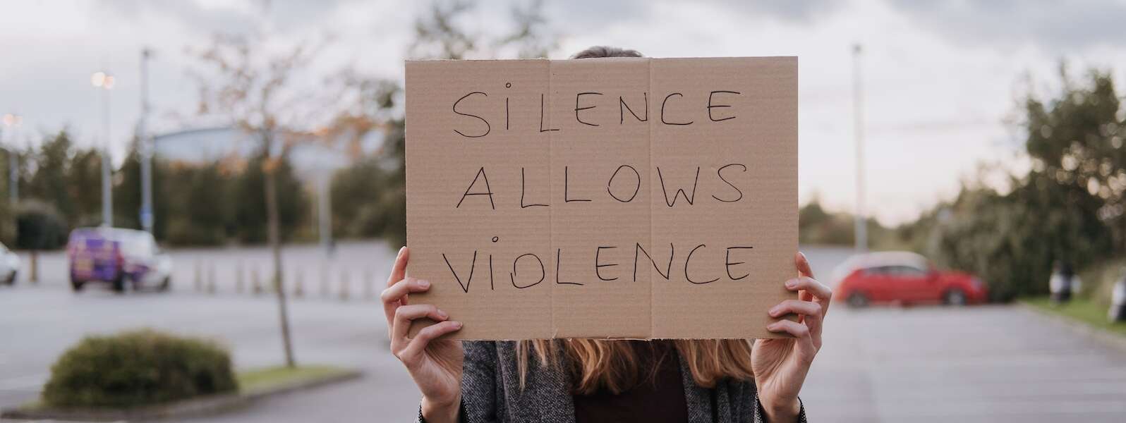 Unrecognizable woman in casual clothes standing on road and demonstrating poster Silence Allows Violence