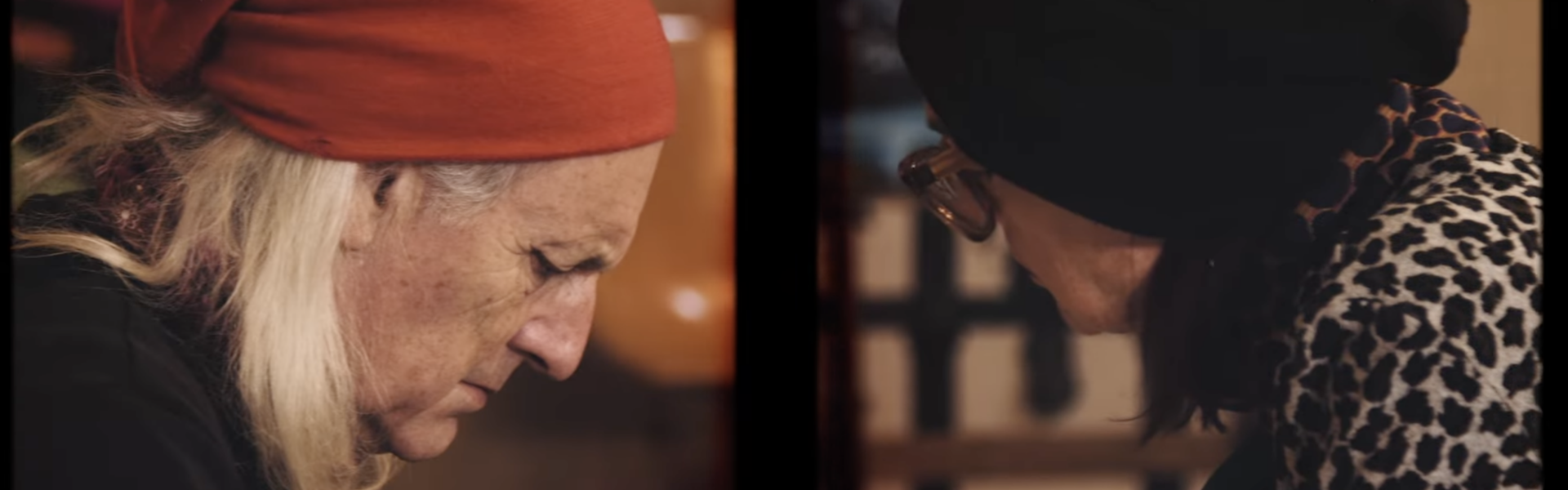 Person in red bandana facing right concentrates on work while opposite them is a person in a black head scarf and glasses facing down.