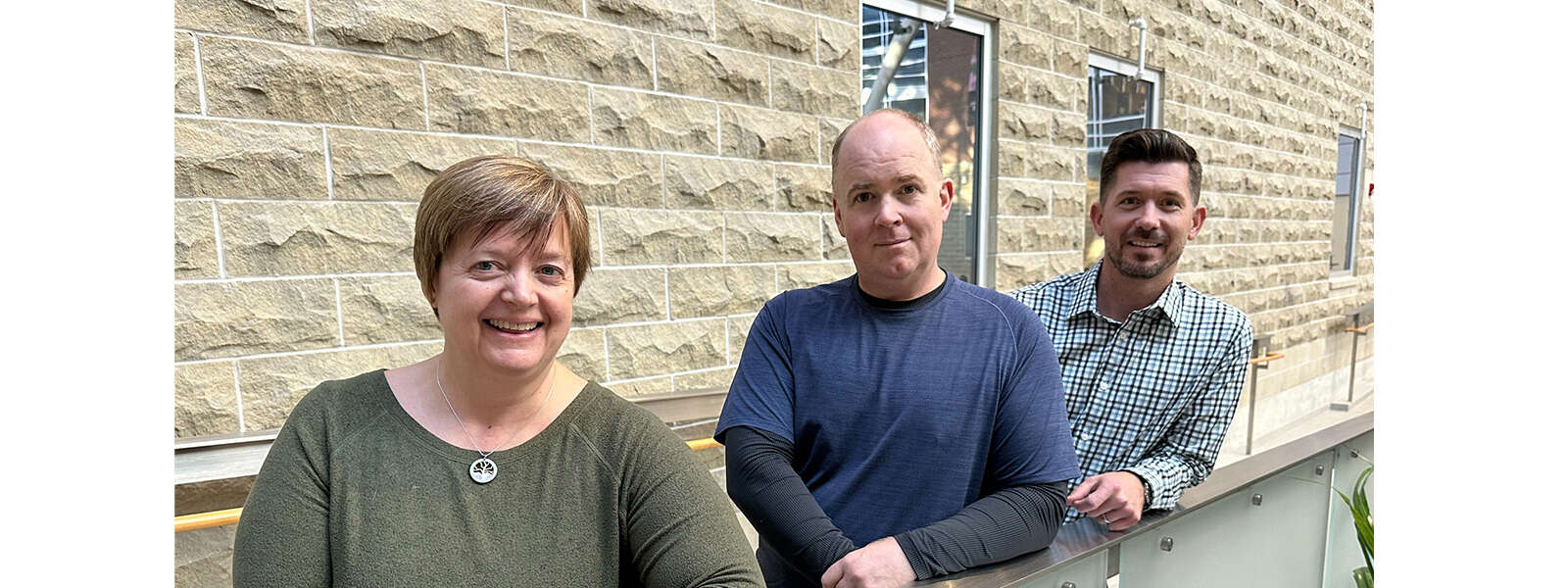 Three people stand near a wall in the Summerlea Science Complex atrium