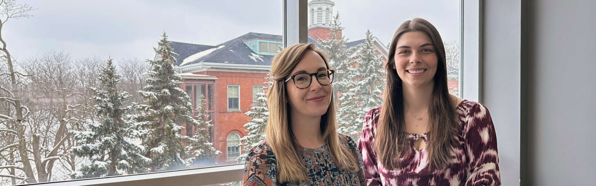 two women at a window with snow-covered trees behind