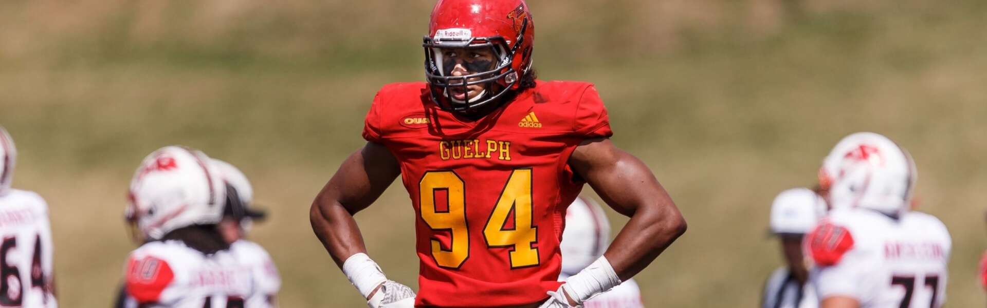 a football player in a red Gryphons uniform surveys the fiedl with other players behind him