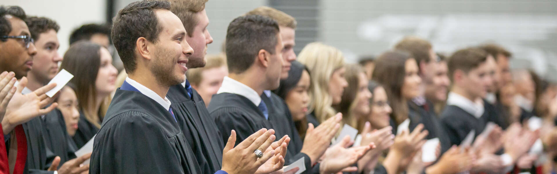 a line of students in convocation regalia smile and applaud