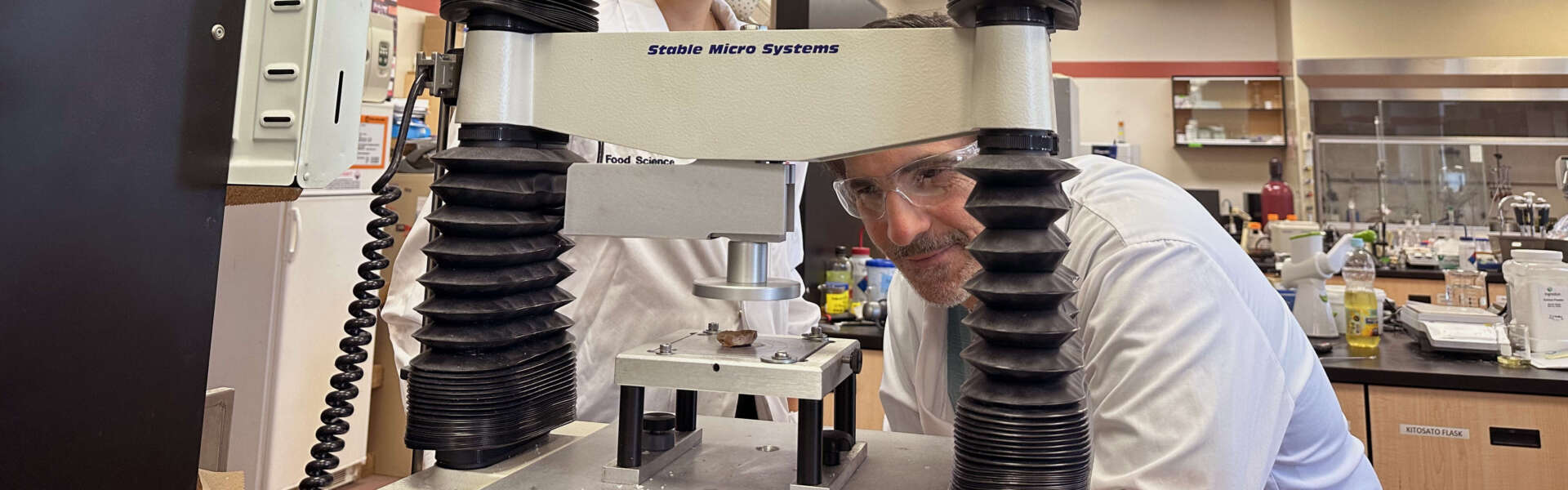 Two people in white lab coats peer through a machine known as a mechanical mouth