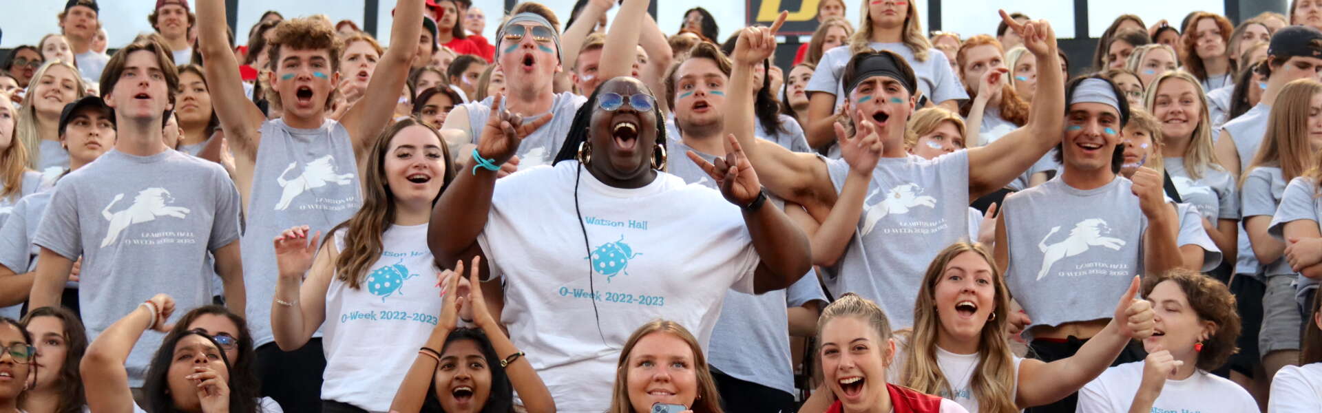 Bleachers fille dwith dozens of excited students waving their hands in the air and smiling for the camera