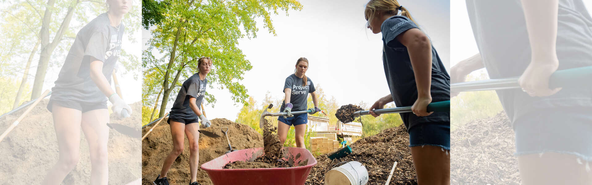 Three students in matching t shirts that say Project Serve shovel dirt into a red wheelbarrow.