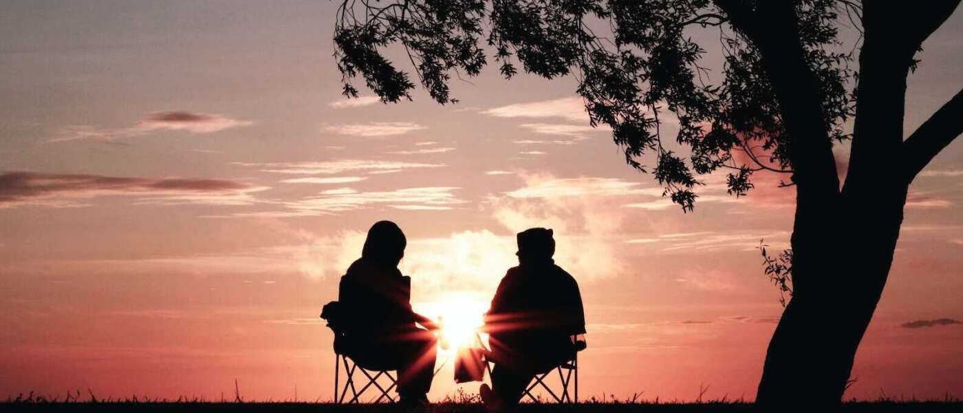 silhouette of two person sitting on chair near tree