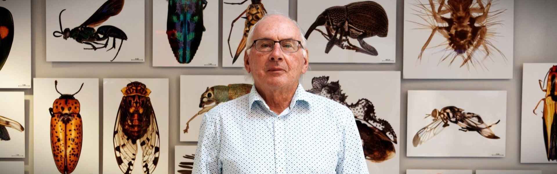 Dr. Paul Hebert poses for a portrait in the atrium of the Centre for Biodiversity Genomics at the University of Guelph with canvas prints of magnified photos of insects hanging on the wall behind him