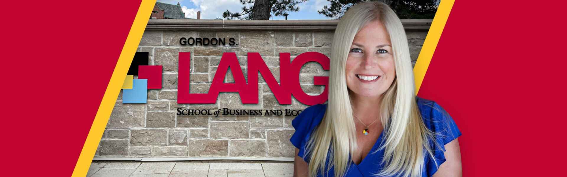 Dr. Sara Mann in front of the Gordon S. Lang School of Business and Economics brick wall sign.