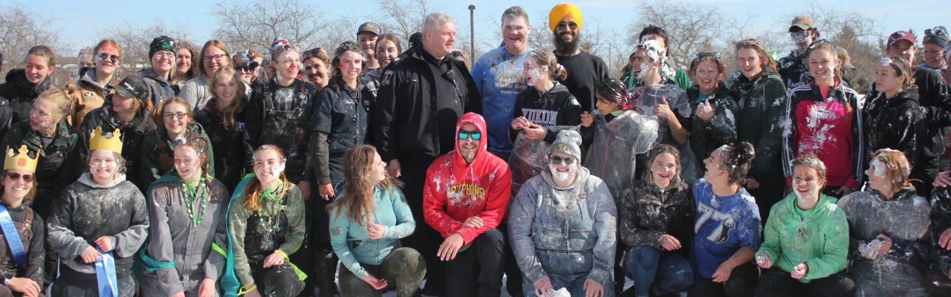 Group of about 35 students smiling on a winter field, some wearing crown and ribbon