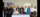 Two people sit at a table with a document with 10 others standing behind with banners for U of G and GGH behind them