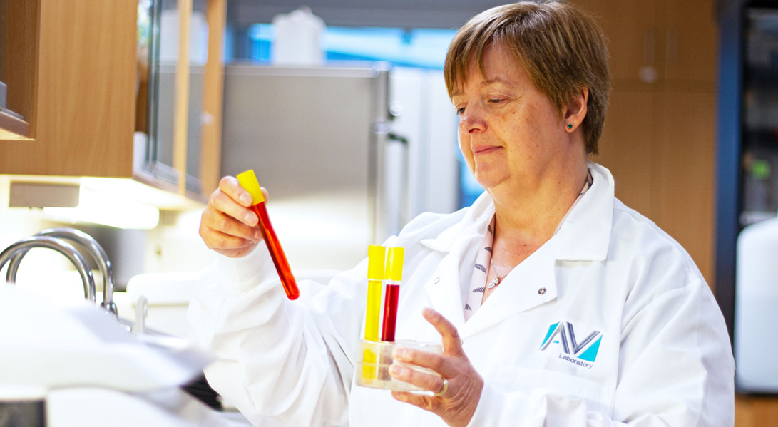 A person in a lab coat stands in a lab and pulls out test tubes filled with coloured liquids from a tube holder