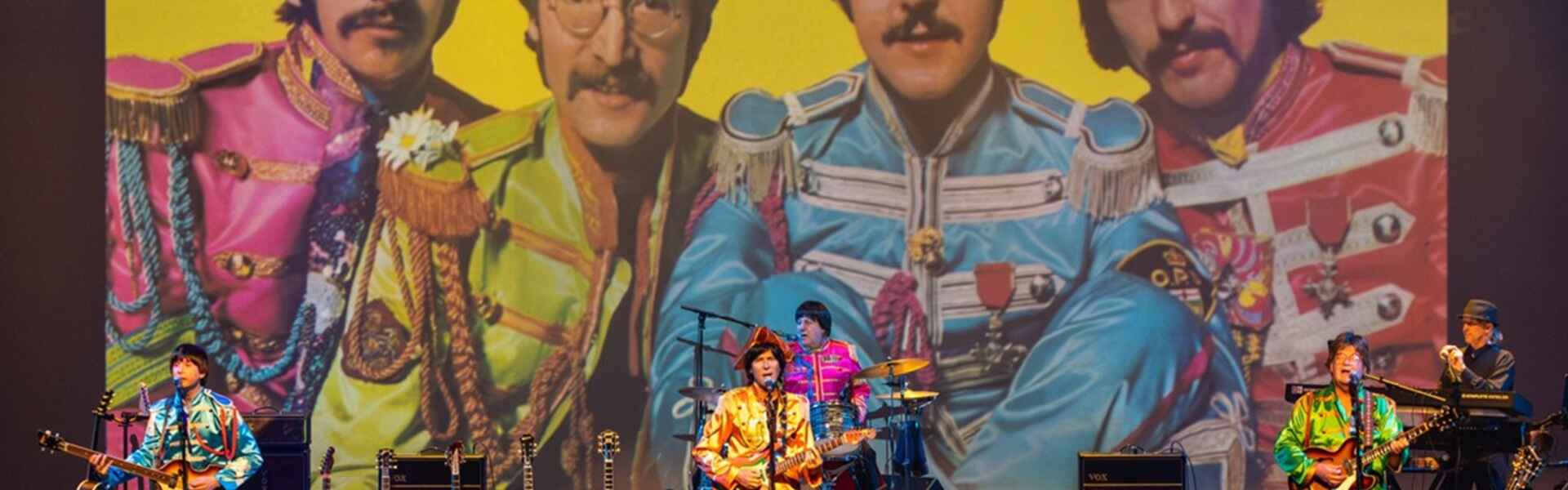A beatles tribute band plays in front of a large image of the original beatles.