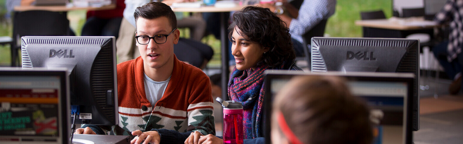 Two students in a computer lab, both examining a screen