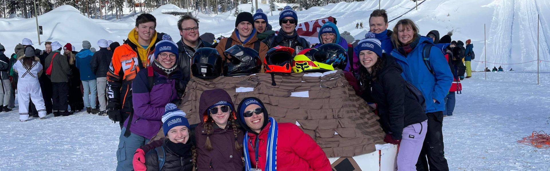 a group of students in winter gear pose for a group photo with a toboggan
