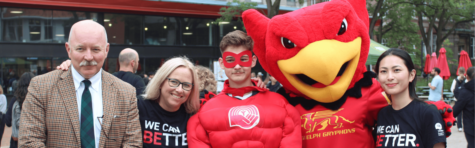 A group of five volunteers for the United Way campaign. Two wear "We can better" shirts, one wears a red superhero costume and one wears a Guelph Gryphons costume.
