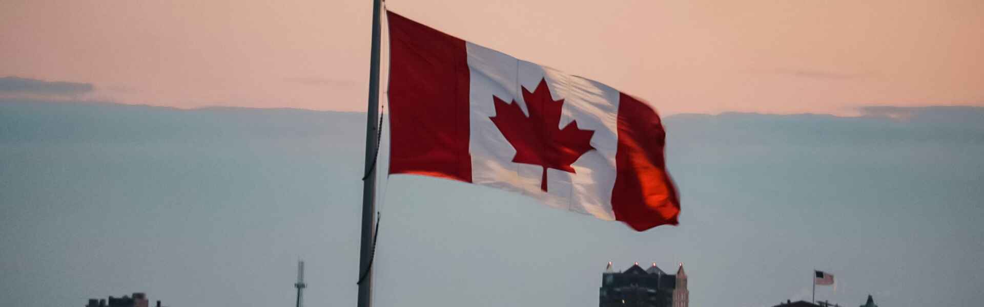 A Canadian flag against an urban background at dusk