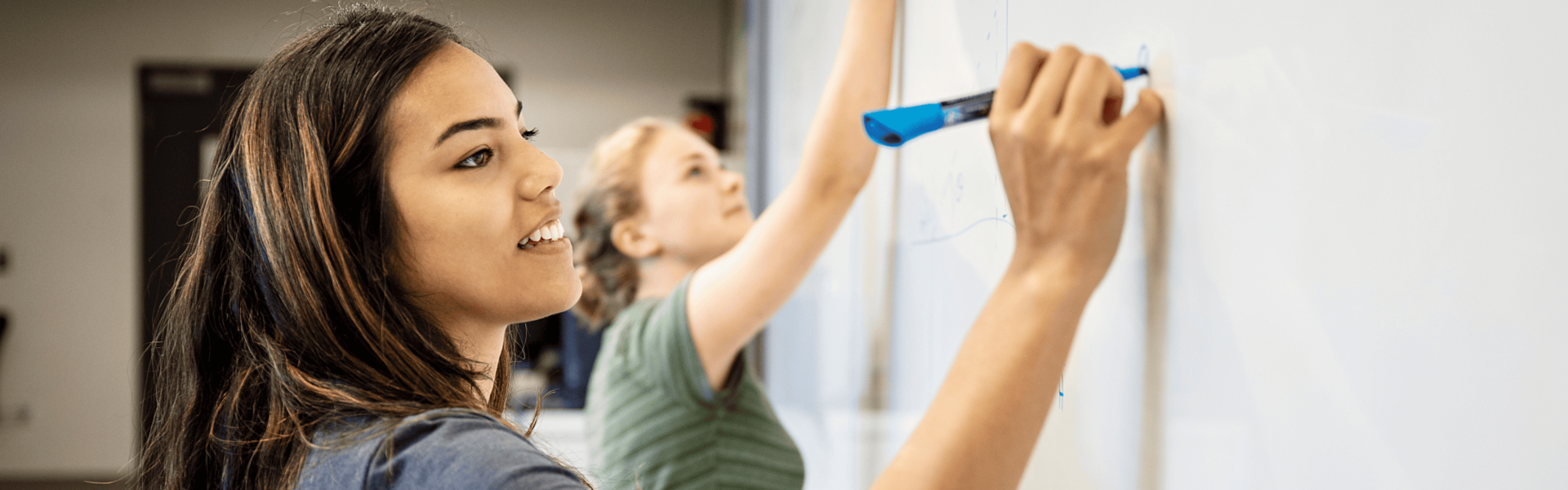Two students draw on a white board