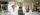 Three researchers wearing white lab coats stand together in a laboratory setting, smiling at the camera. The researcher on the left has short, styled hair and is wearing purple gloves. The researcher in the middle wears glasses and a plaid shirt under their lab coat. The researcher on the right has long brown hair and a black shirt under their lab coat. Laboratory equipment and shelves are visible in the background.