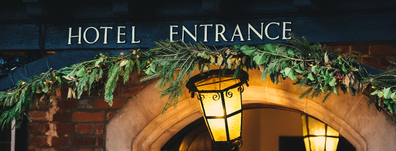 Hotel entrance sign framed by evergreen garland and warm lantern light.