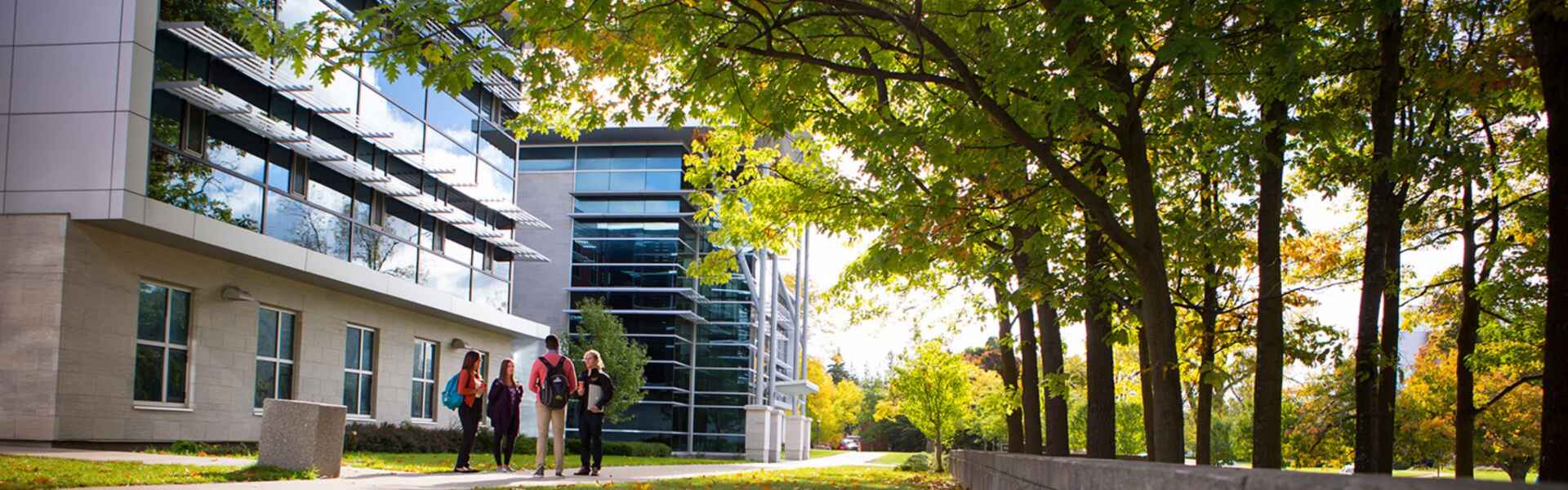 A group of four students stand and chat in front of a building on the U of G campus.