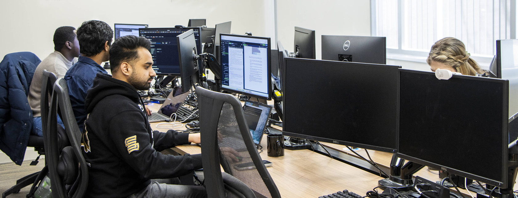 Five people work at a large computer station