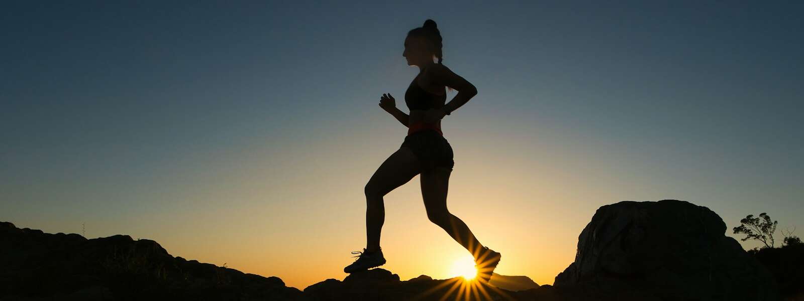 silhouette of man jumping on rocky mountain during sunset