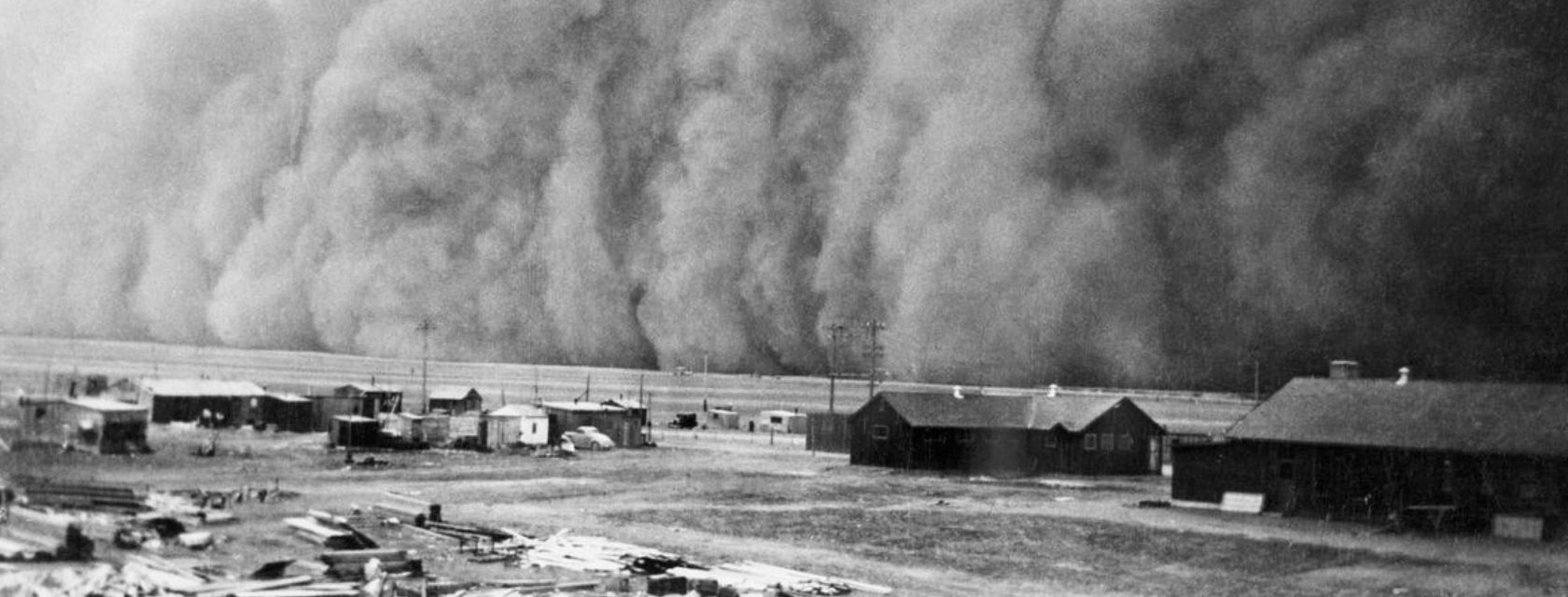 black and white photo showing dusty sky over farm buildings
