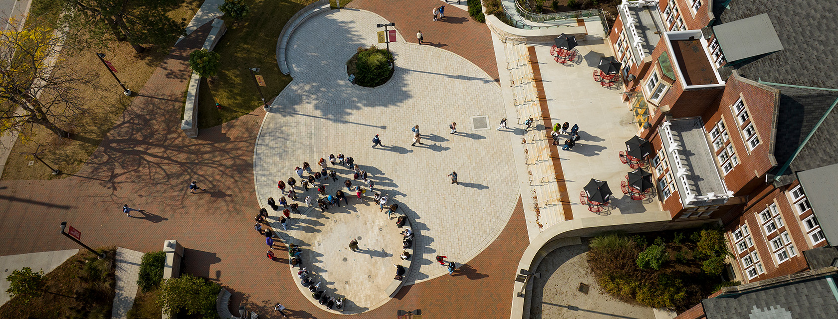 An aerial view of a red brick building and brick plaza with several people gathered in a circle