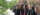 The backs of the heads of several grads in robes walking on a tree-lined path on a sunny day